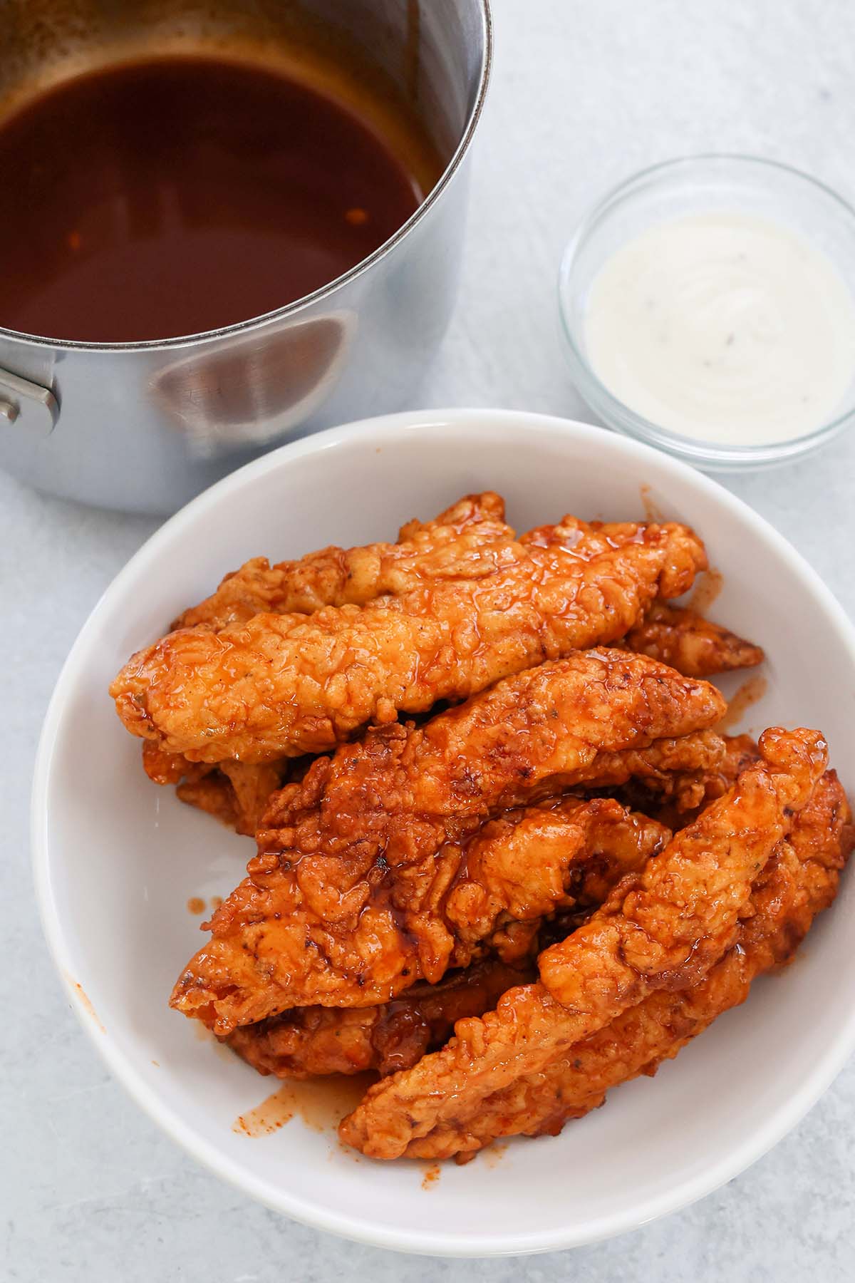 hot honey chicken tenders on a white plate with sauces on the side. 