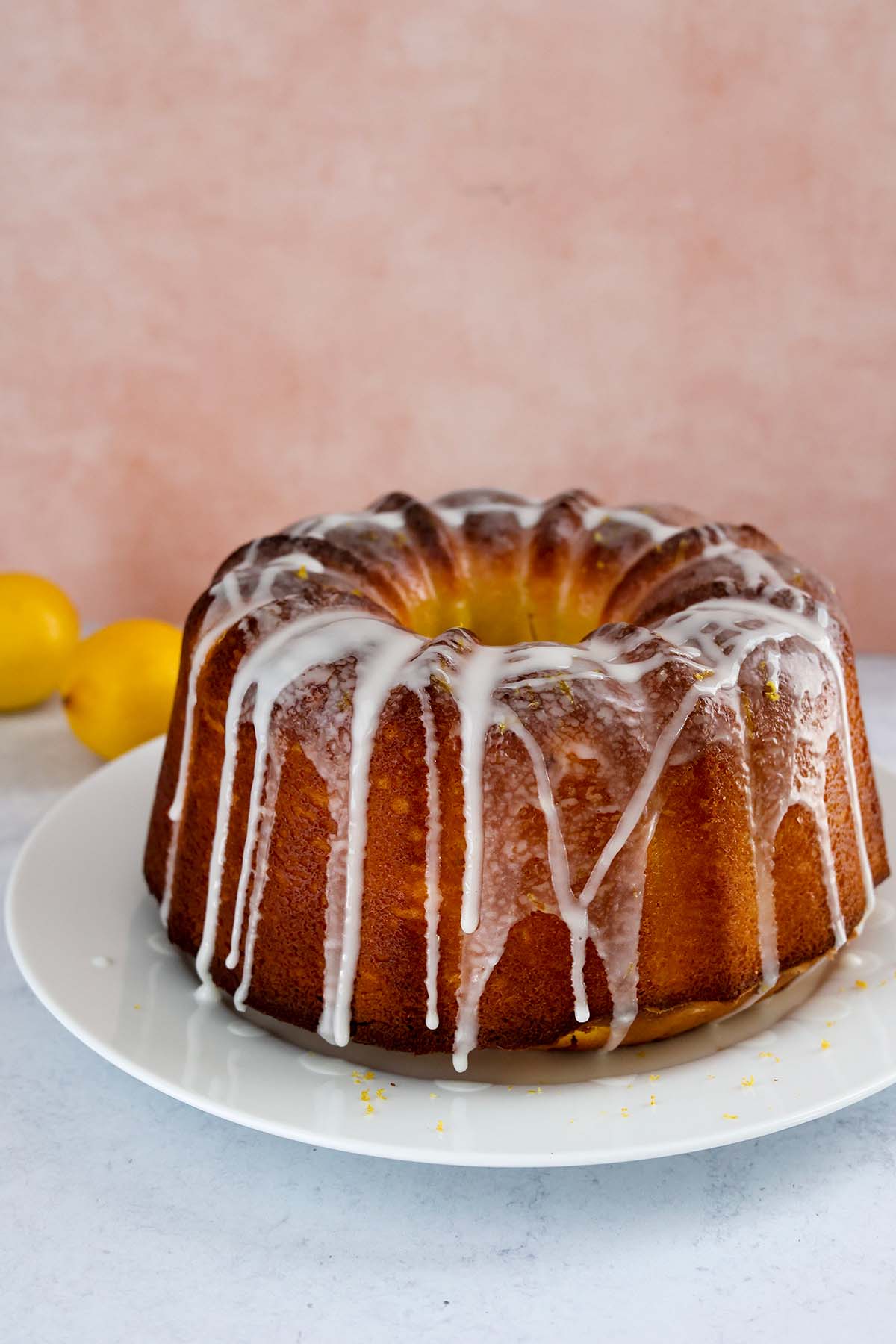 Entire cake on a white plate with lemons in the background. 