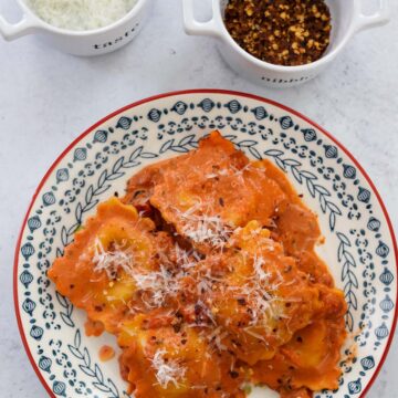 lobster raviolis and sauce on a plate with parmesan cheese and red crushed pepper on the side.