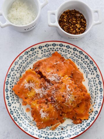 lobster raviolis and sauce on a plate with parmesan cheese and red crushed pepper on the side.