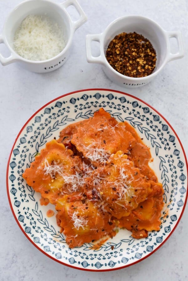 lobster raviolis and sauce on a plate with parmesan cheese and red crushed pepper on the side.