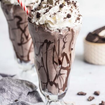 Oreo cookie milkshake with whipped cream and a red and white straw.
