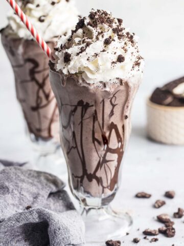 Oreo cookie milkshake with whipped cream and a red and white straw.