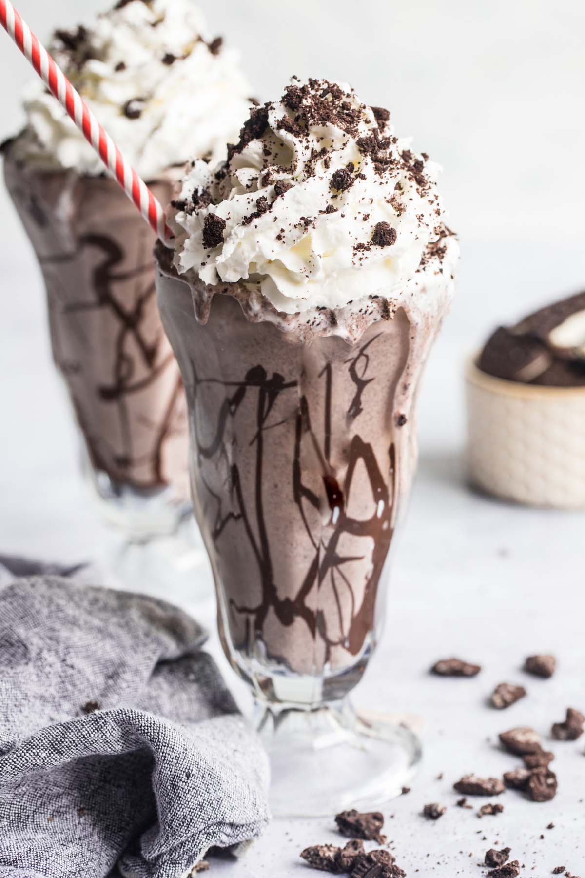 Oreo cookie milkshake with whipped cream and a red and white straw.