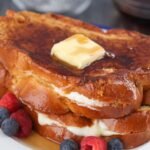 two stuffed french toasts with butter, syrup, and berries.
