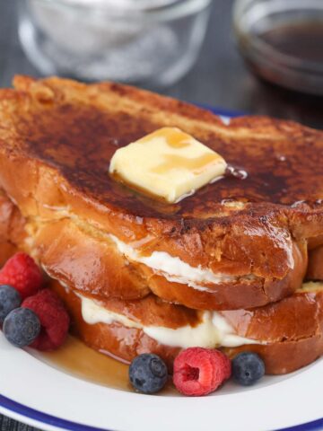 two stuffed french toasts with butter, syrup, and berries.