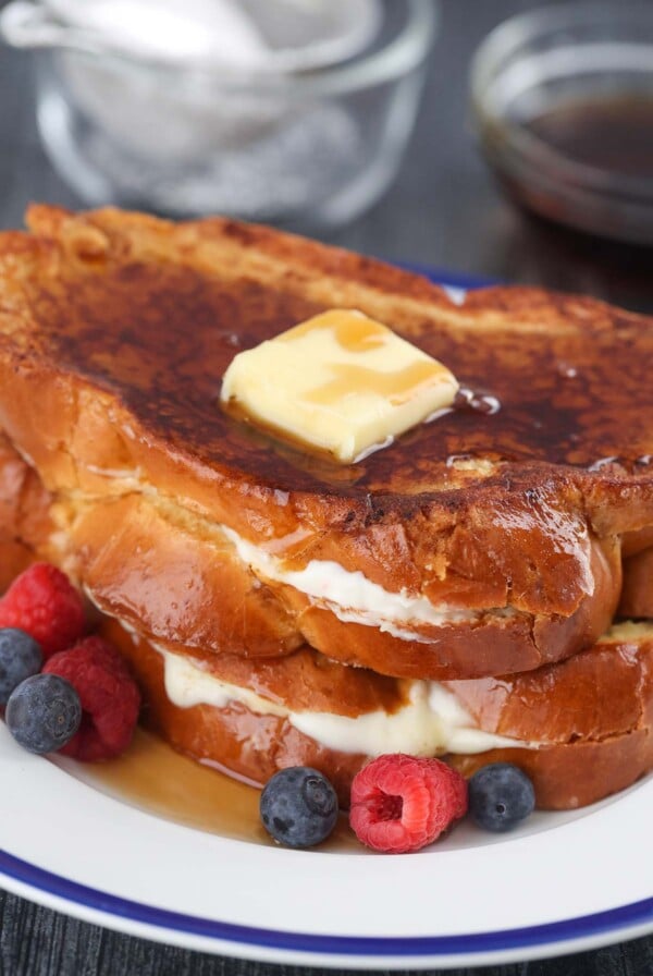 two stuffed french toasts with butter, syrup, and berries.