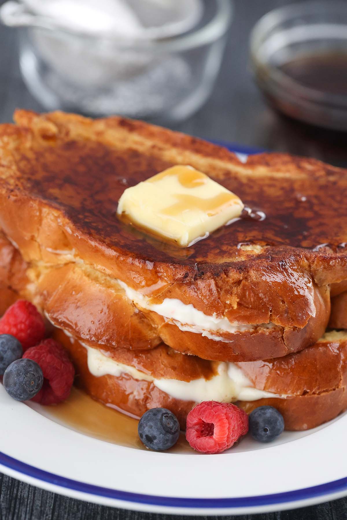 two stuffed french toasts with butter, syrup, and berries. 