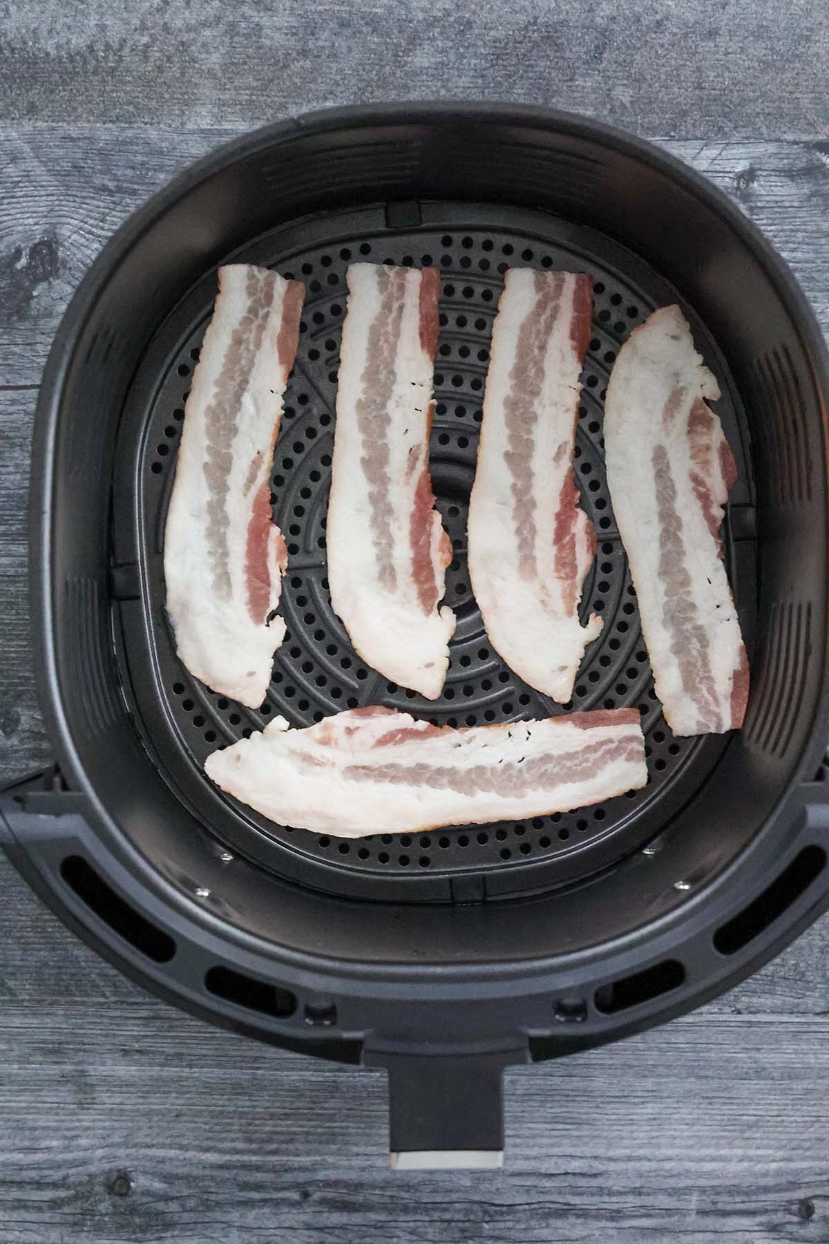 four raw bacon strips in the air fryer basket.