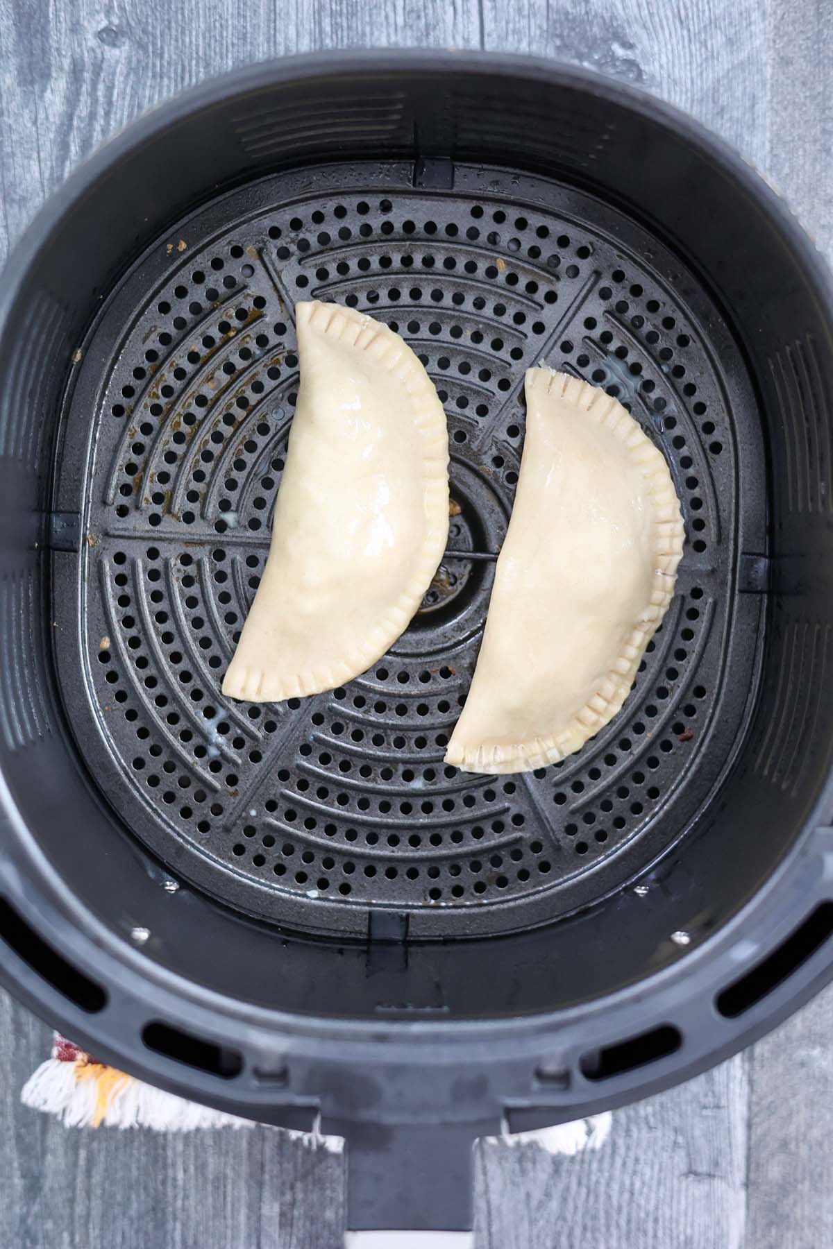 two uncooked empanadas in the air fryer basket. 
