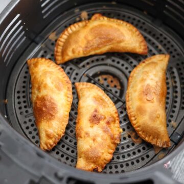 four cooked ground beef empanadas in the air fryer basket.