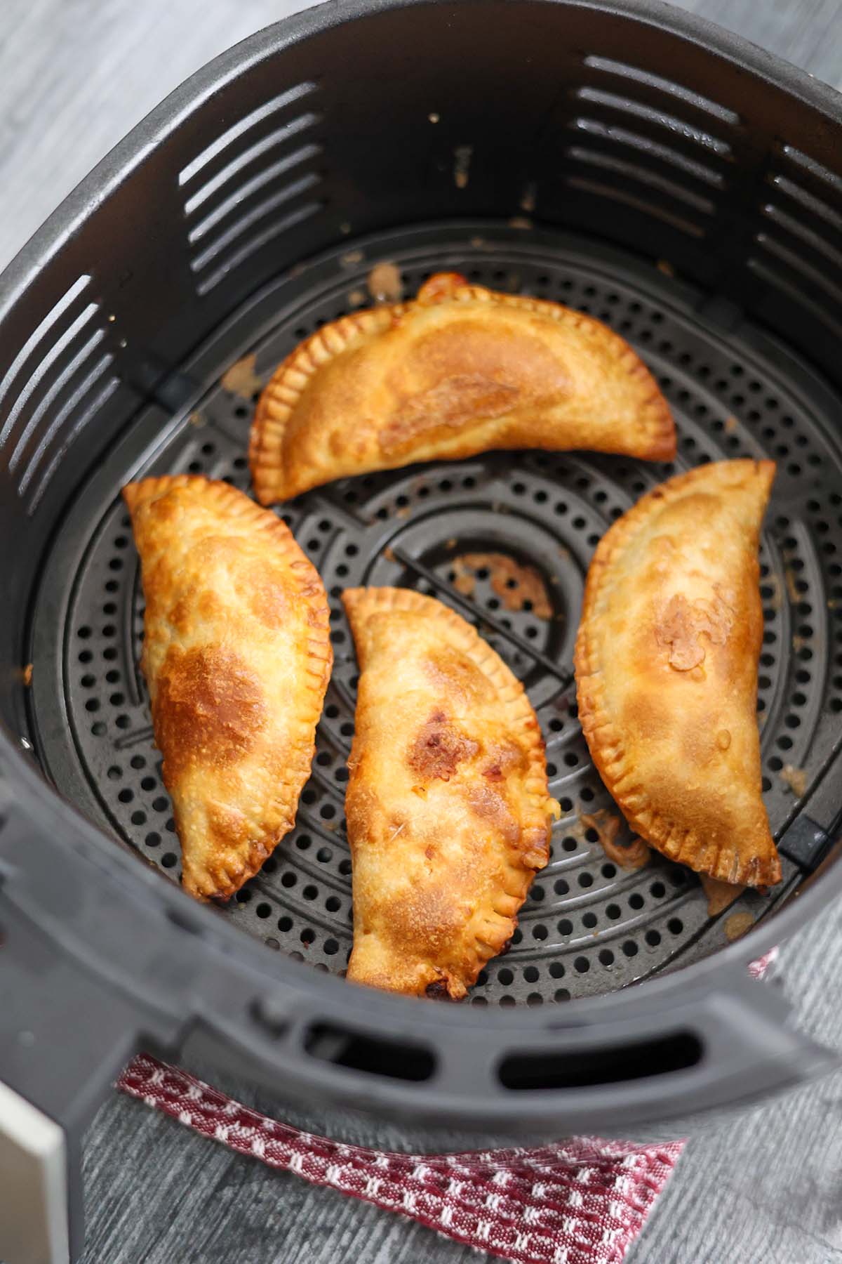 four cooked ground beef empanadas in the air fryer basket. 