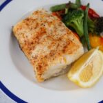 baked chilean sea bass with a lemon wedge and mixed vegetables.