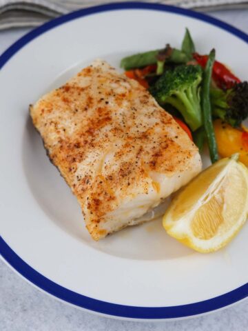 baked chilean sea bass with a lemon wedge and mixed vegetables.