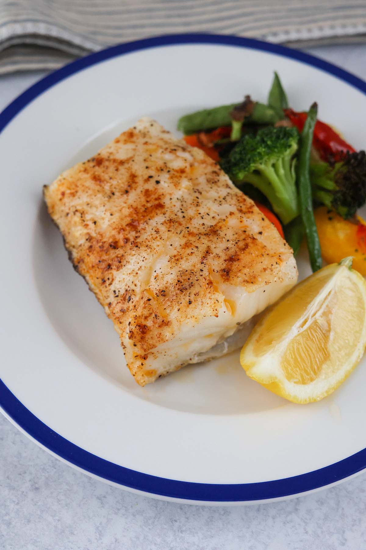 baked chilean sea bass with a lemon wedge and mixed vegetables. 