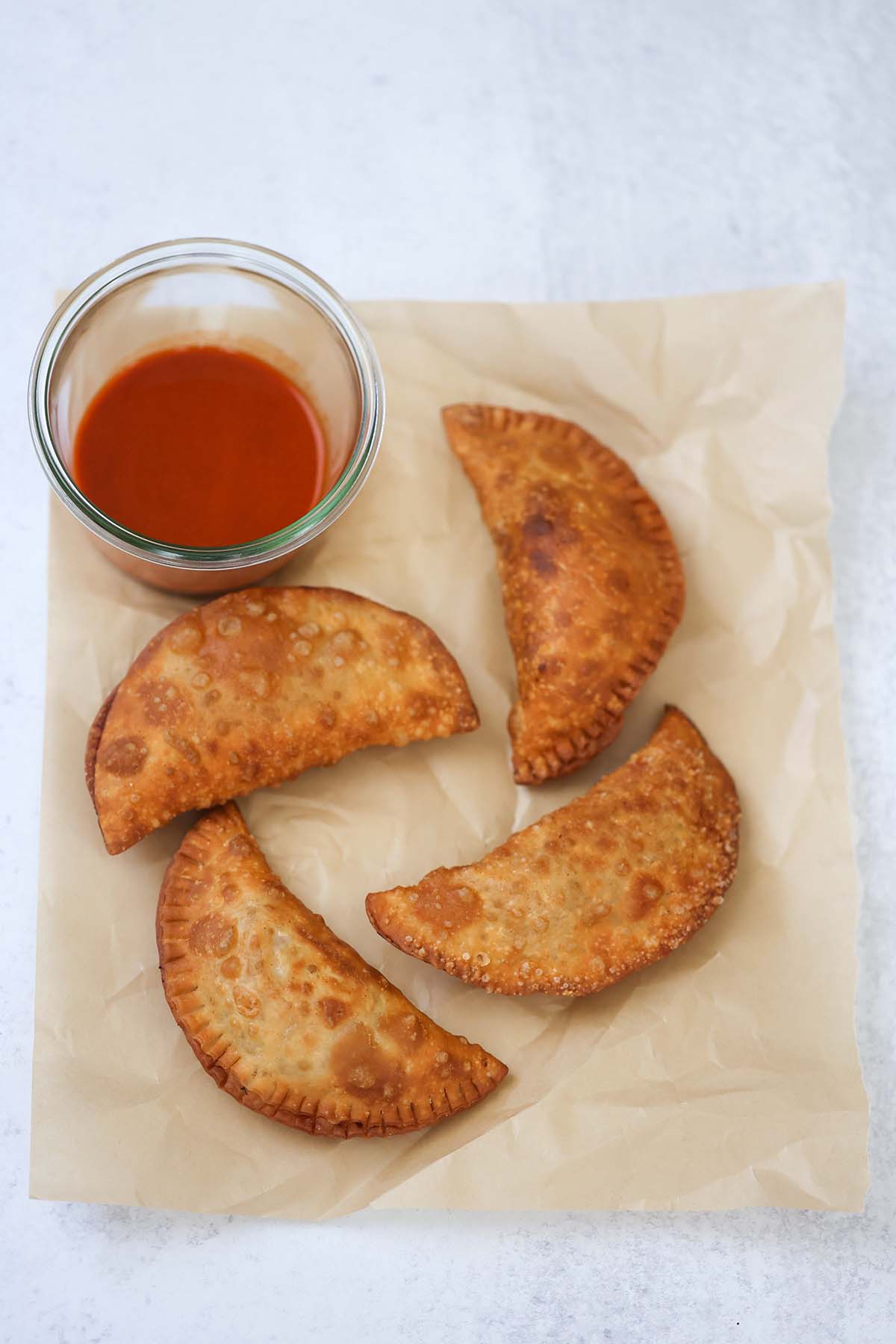 four fried chicken empanadas with hot sauce on the side. 