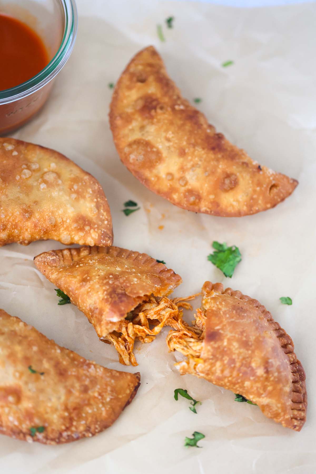 four chicken empanadas with hot sauce on the side. 