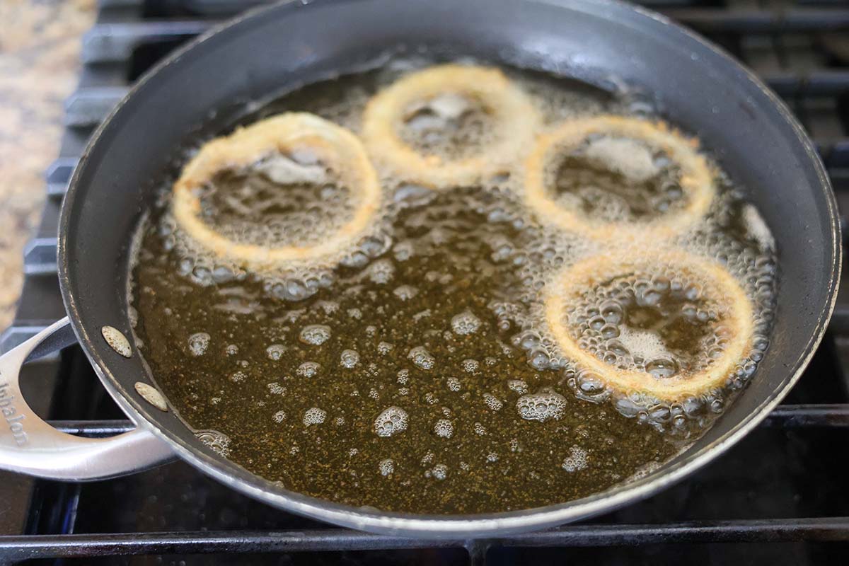 four onion rings frying in a skillet with oil. 