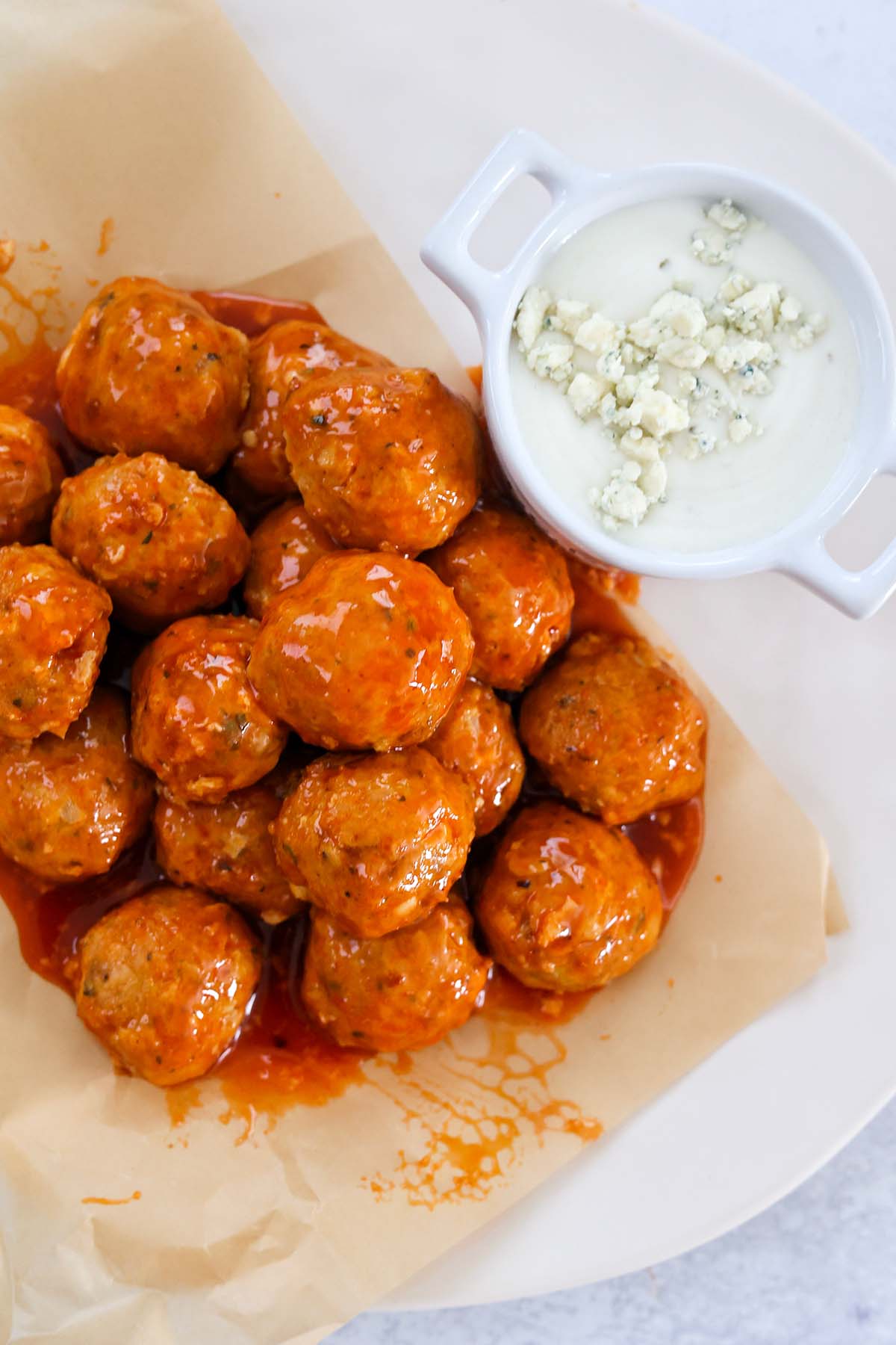 honey buffalo coated chicken meatballs on a plate with blue cheese dip on the side. 