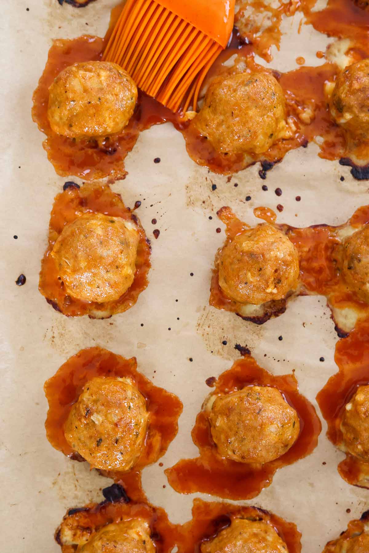 baked meatballs on a baking sheet with a pastry brush.