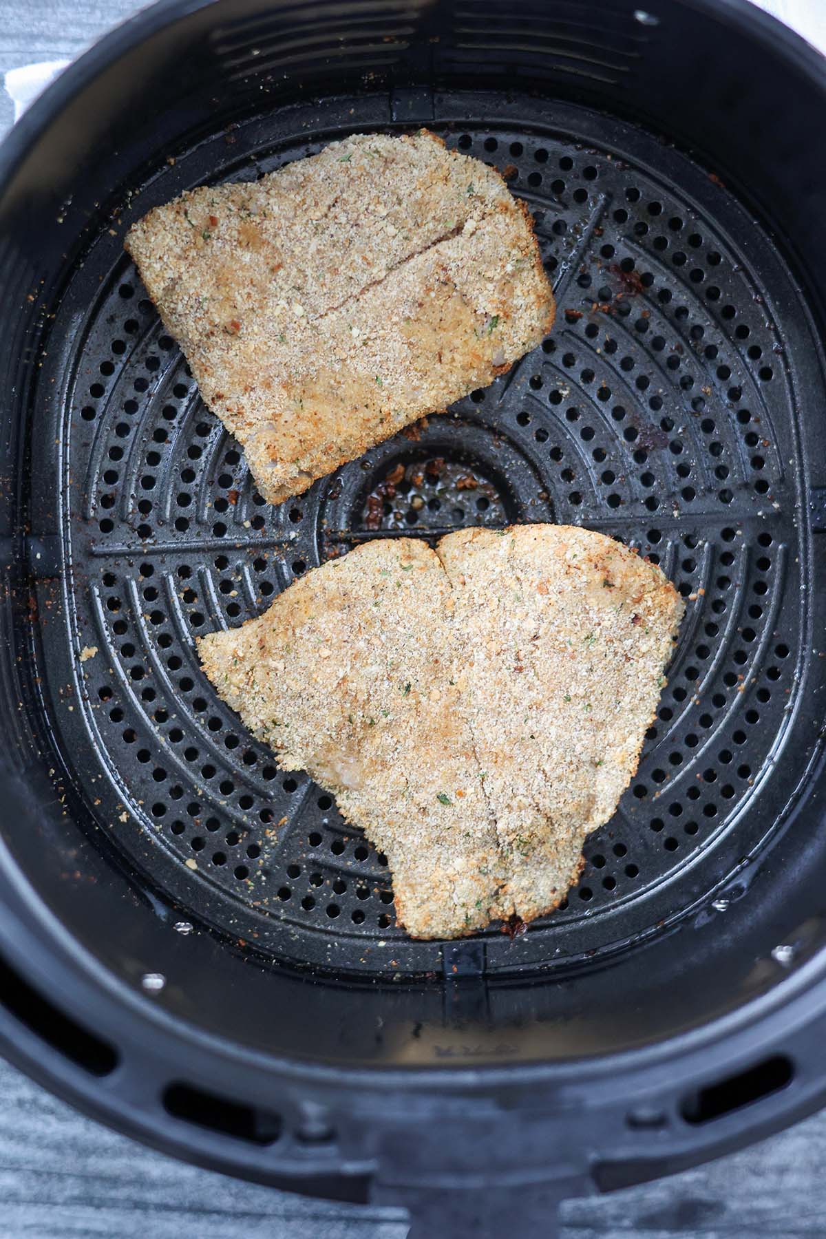 two breaded grouper fillets in the air fryer basket. 