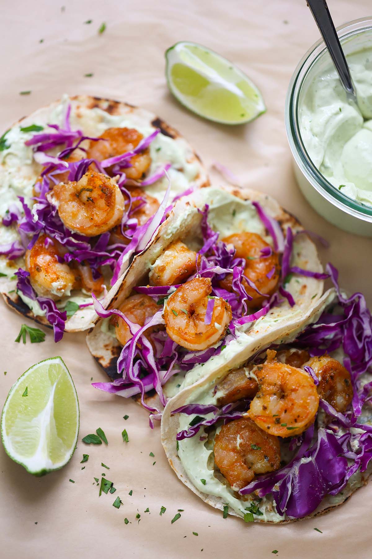 Three air fryer shrimp tacos with limes and avocado crema on the side. 