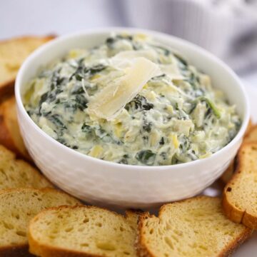 Crockpot spinach artichoke dip in a white bowl with baguette slices.
