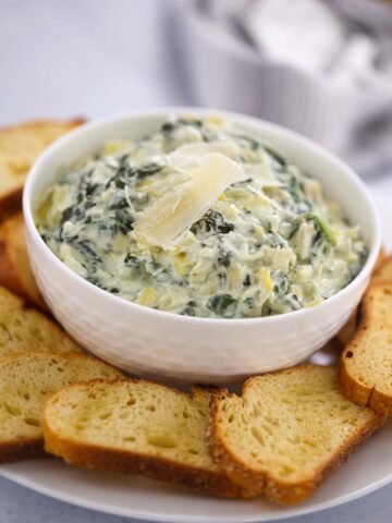 Crockpot spinach artichoke dip in a white bowl with baguette slices.
