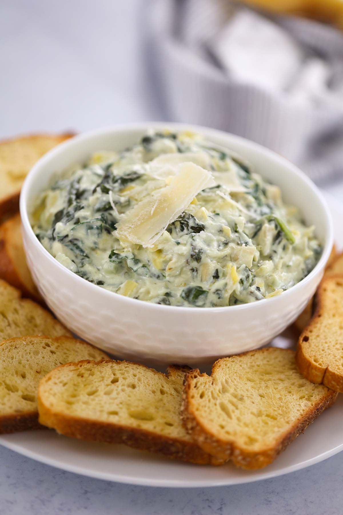 Crockpot spinach artichoke dip in a white bowl with baguette slices. 