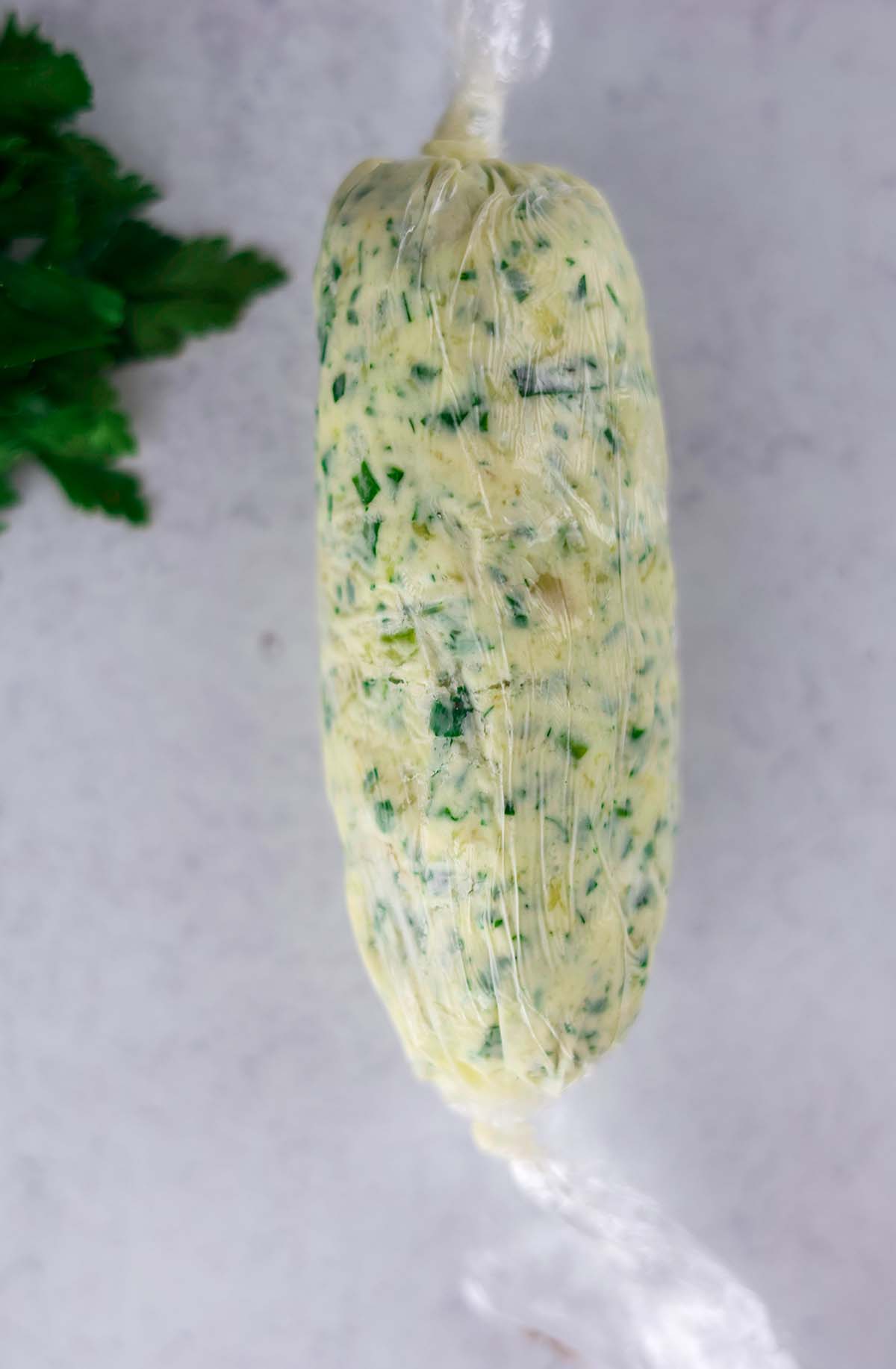 garlic herb compound butter formed into a log in plastic wrap. 