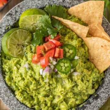 Guacamole in a molcajete topped with limes, tomatoes, jalapenos, and chips.