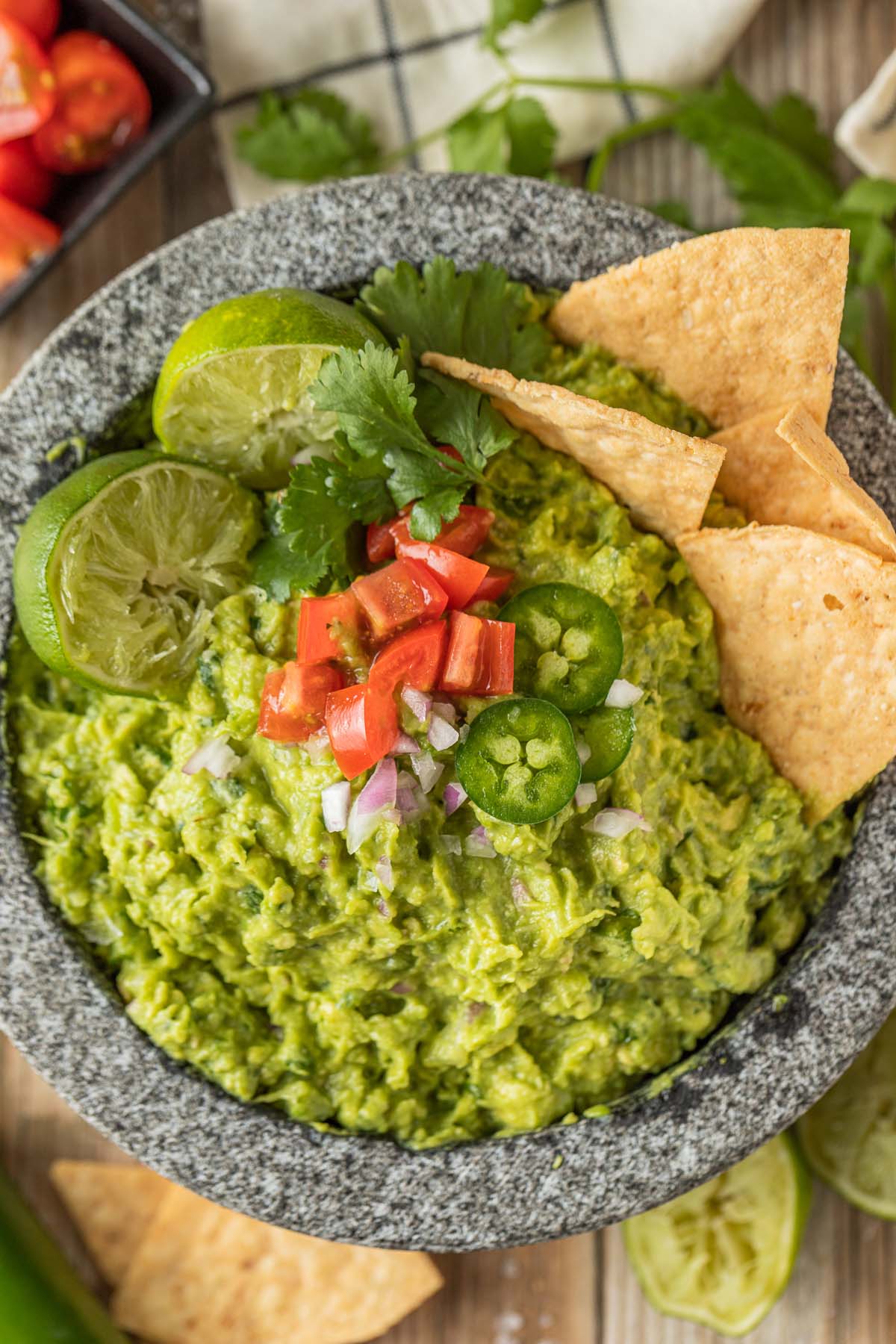 Guacamole in a molcajete topped with limes, tomatoes, jalapenos, and chips. 