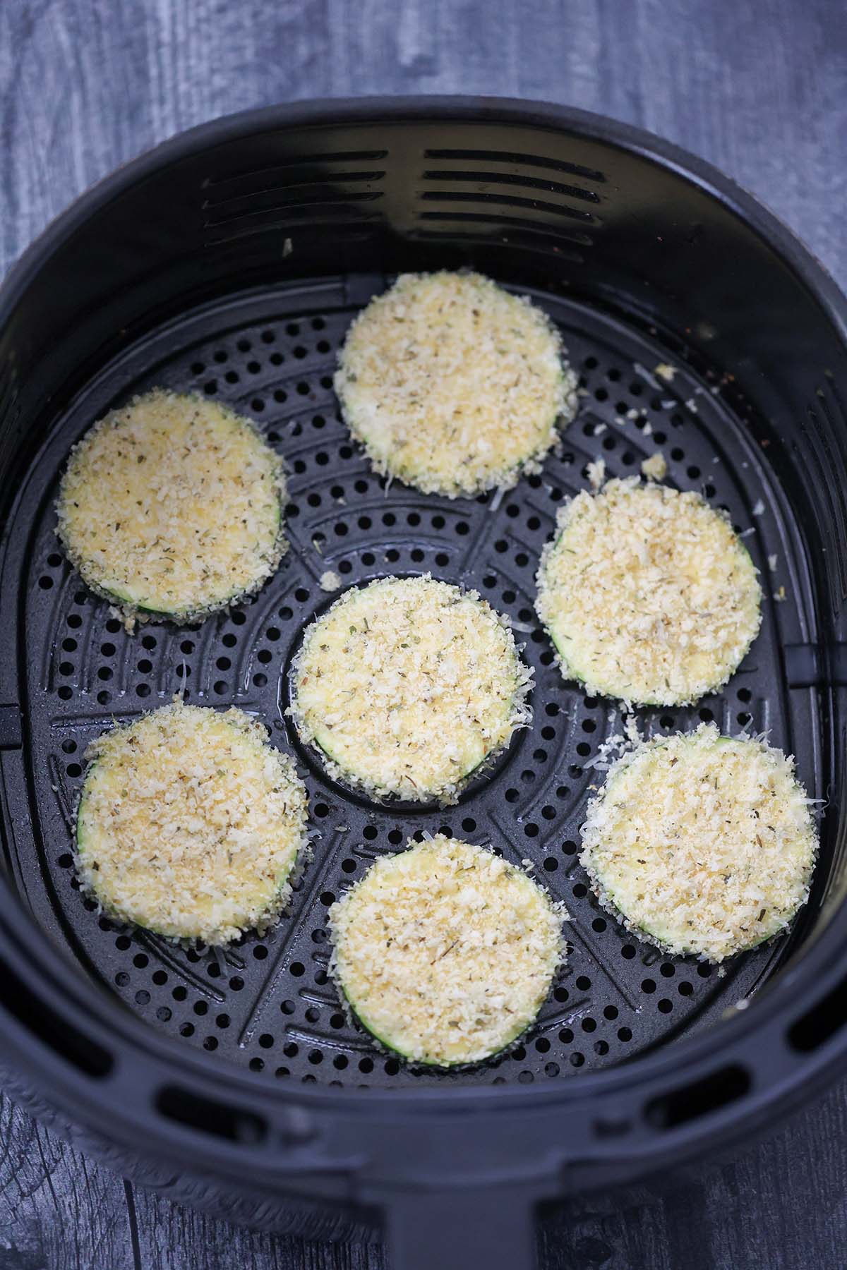 seven raw zucchini chips in the air fryer basket. 