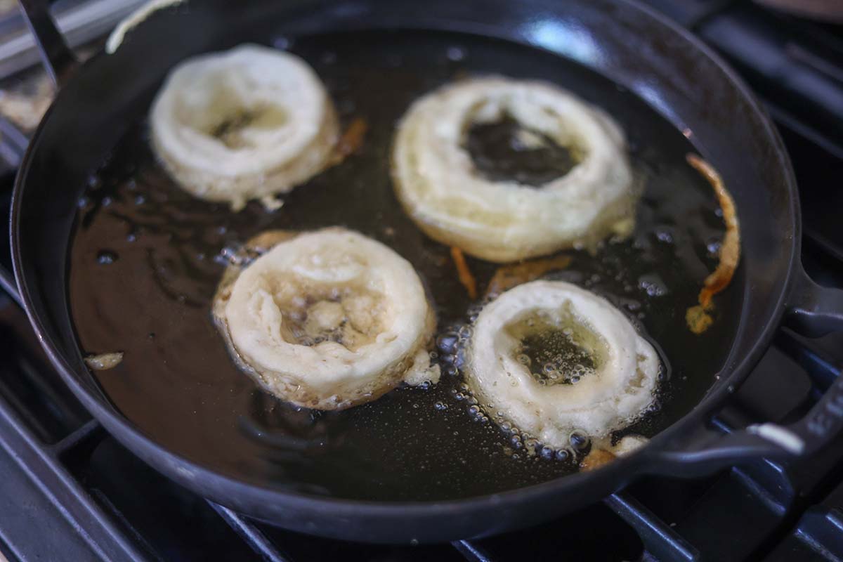 four onion rings frying in a skillet with oil. 