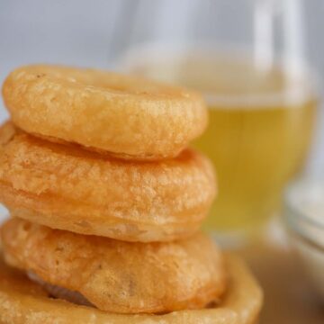 four beer battered onion rings with a glass of beer in the background.