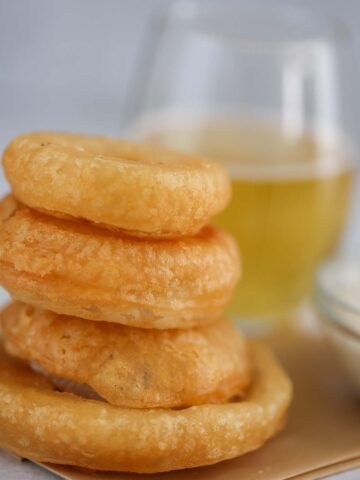four beer battered onion rings with a glass of beer in the background.