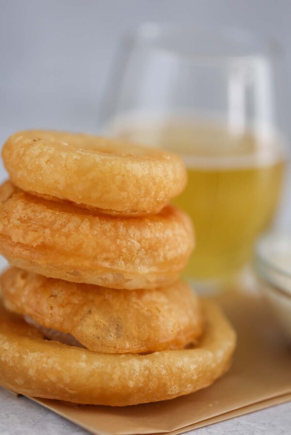four beer battered onion rings with a glass of beer in the background.