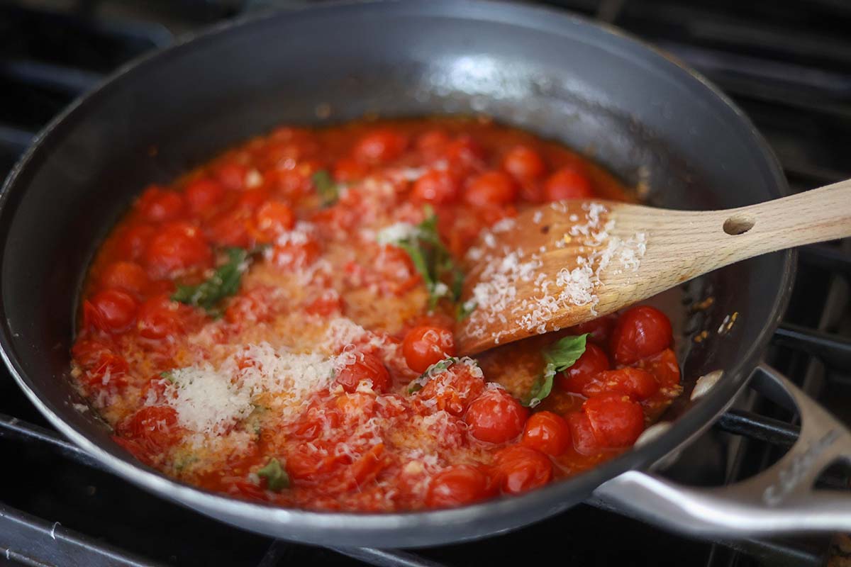 cherry tomatoes, basil, and parmesan cheese in a skillet with a wooden spoon. 