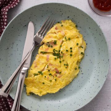 ham and cheese omelet with chives on top and ketchup on the side.