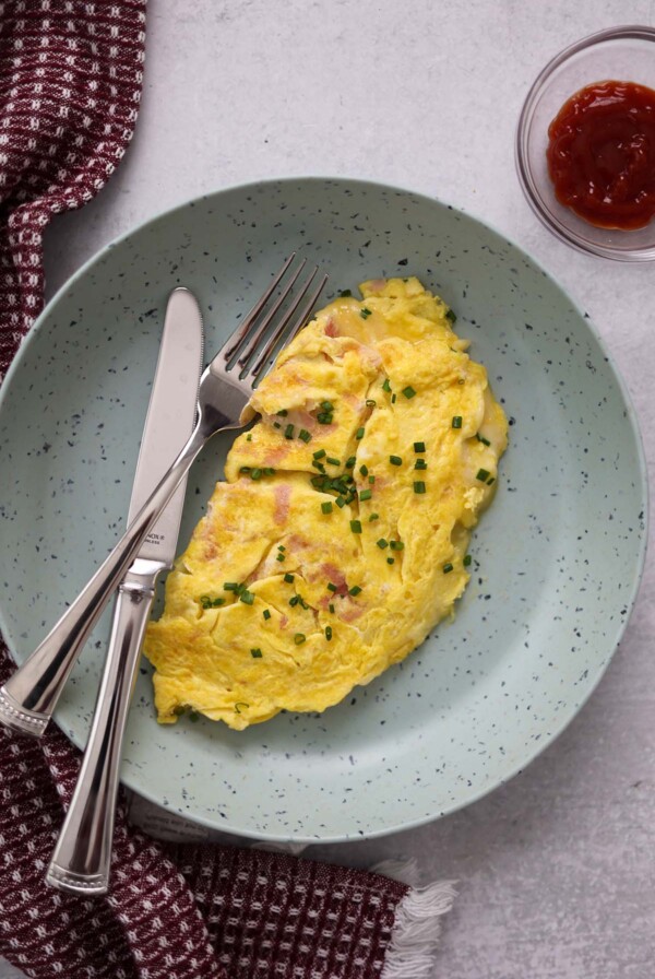 ham and cheese omelet with chives on top and ketchup on the side.