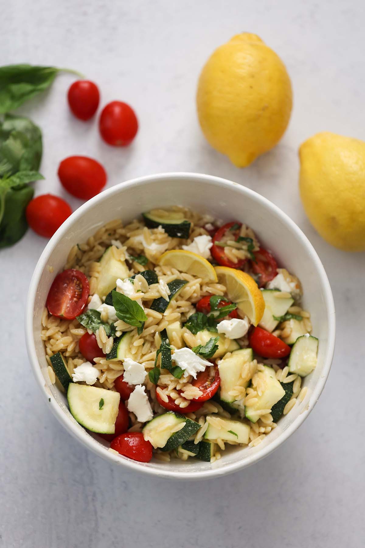 orzo pasta salad with goat cheese, basil, and lemon wedges on top. 