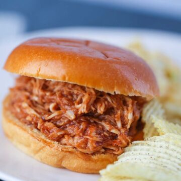 Pulled BBQ chicken sandwich with potato chips on the side.