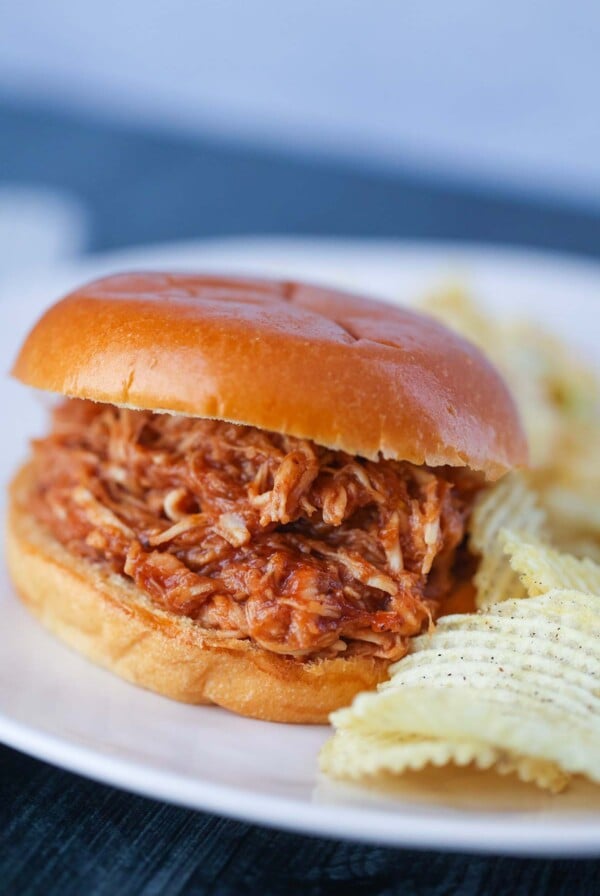 Pulled BBQ chicken sandwich with potato chips on the side.