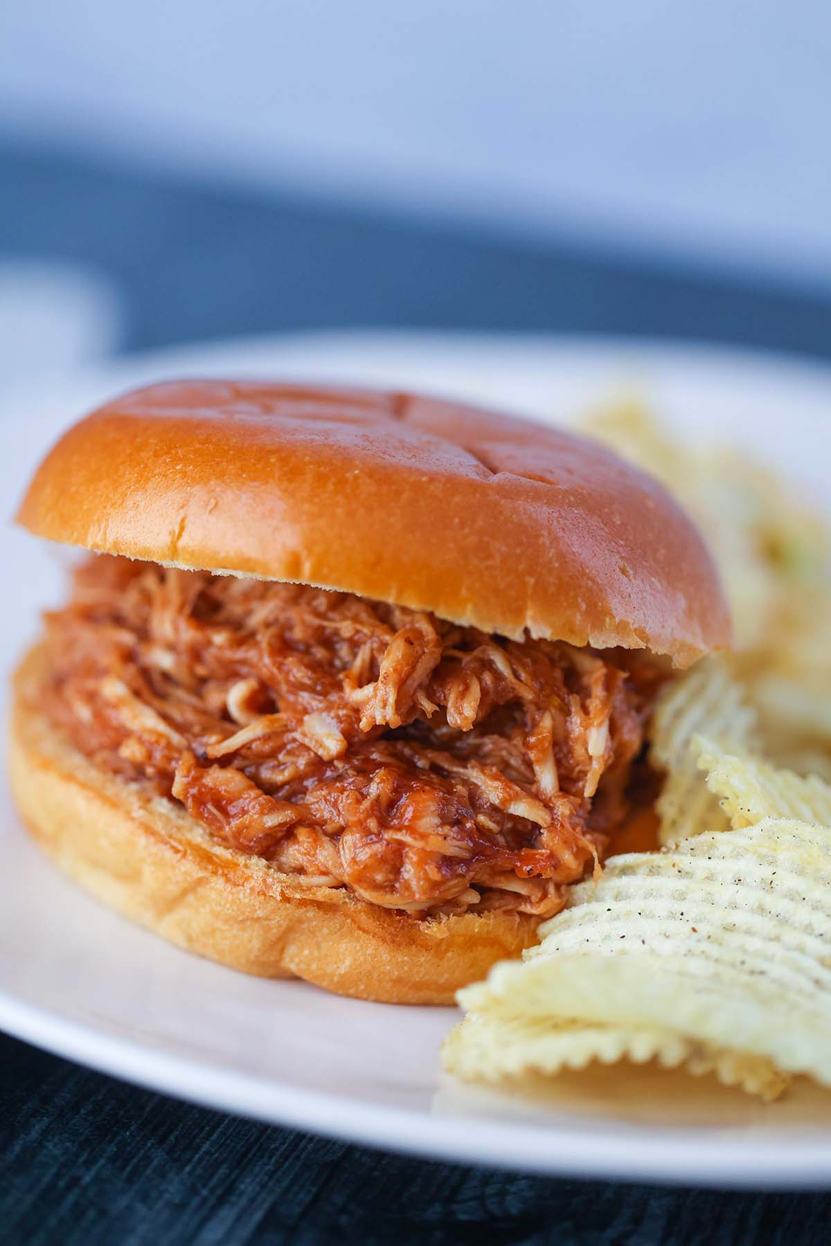 Pulled BBQ chicken sandwich with potato chips on the side. 