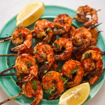 bbq grilled shrimp skewers on a plate with lemon wedges on the side.