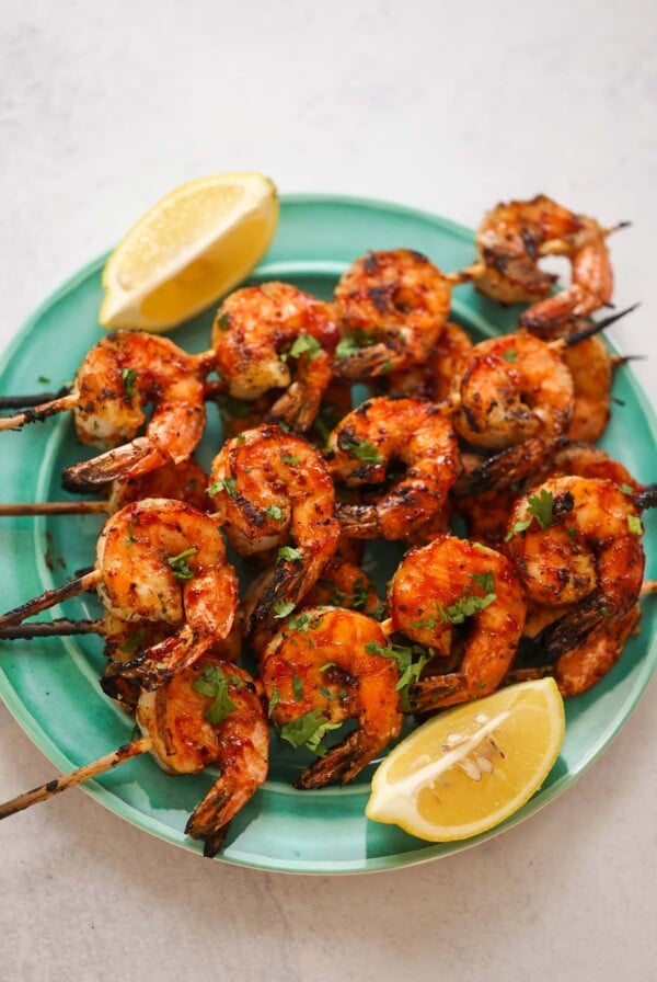 bbq grilled shrimp skewers on a plate with lemon wedges on the side.