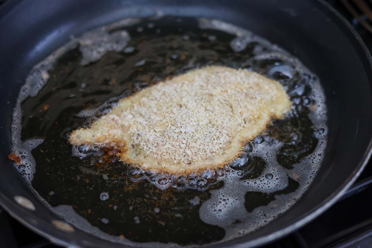 chicken milanese frying in a skillet with oil. 