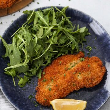 chicken milanese with a lemon wedge and arugula on the side.