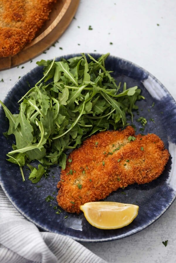 chicken milanese with a lemon wedge and arugula on the side.