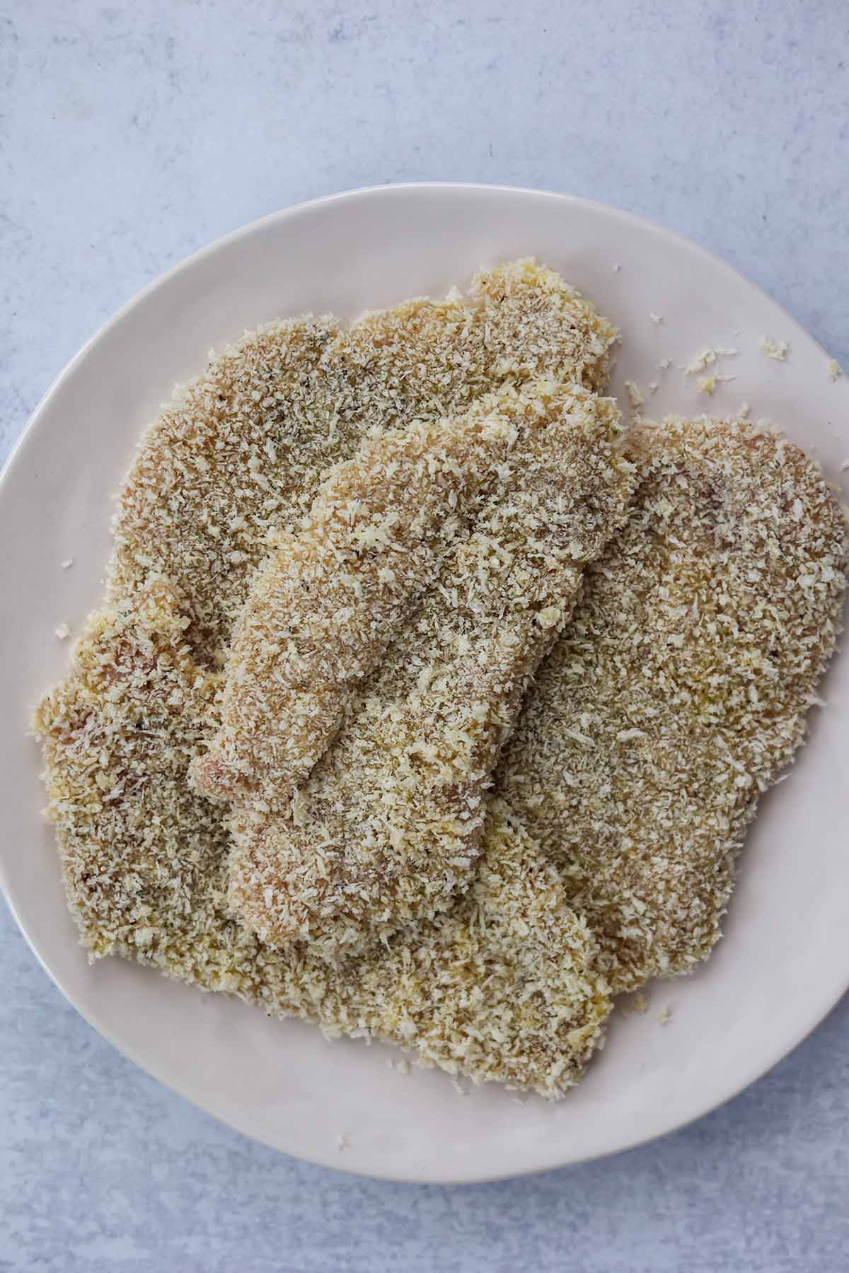 four raw chicken breasts coated in panko breadcrumbs.